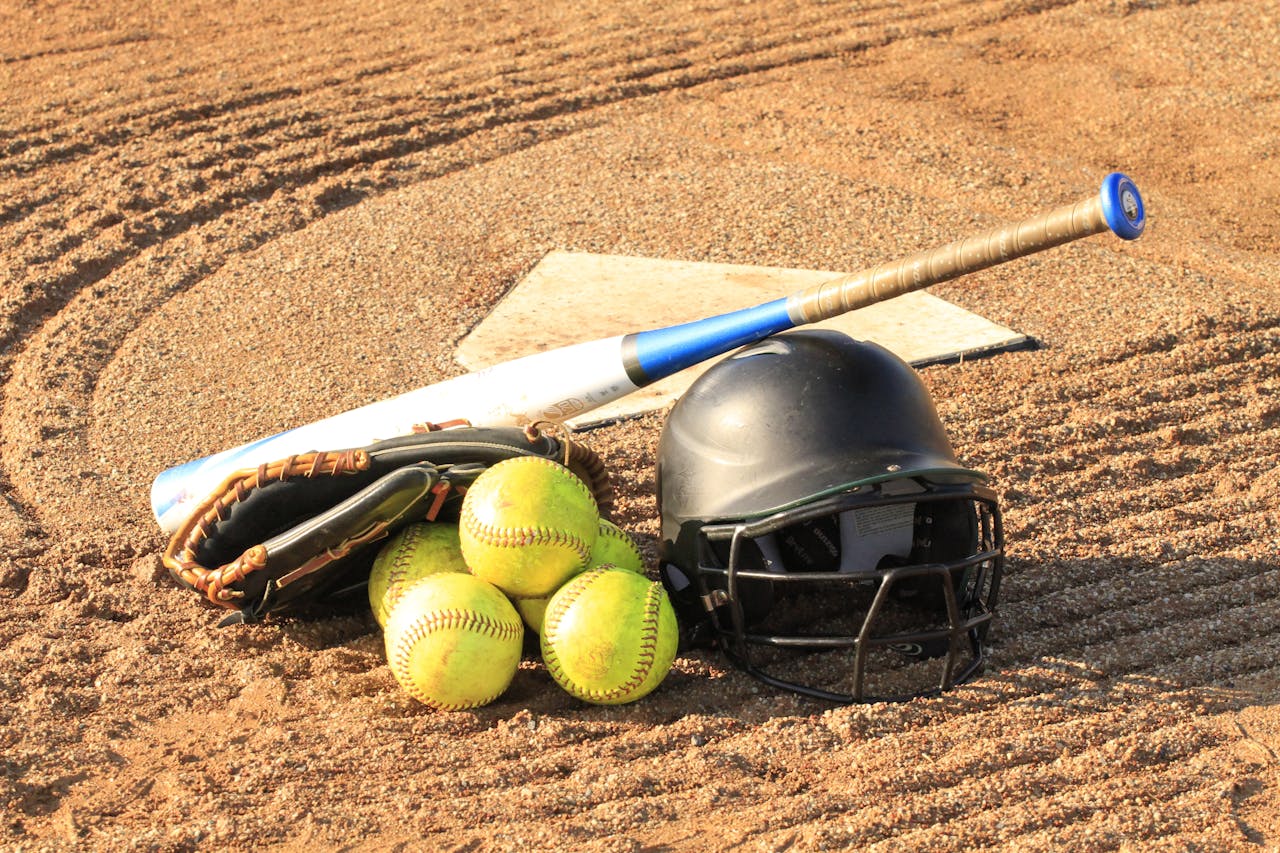 Close-up of baseball and softball gear on a dirt field, ready for a game.